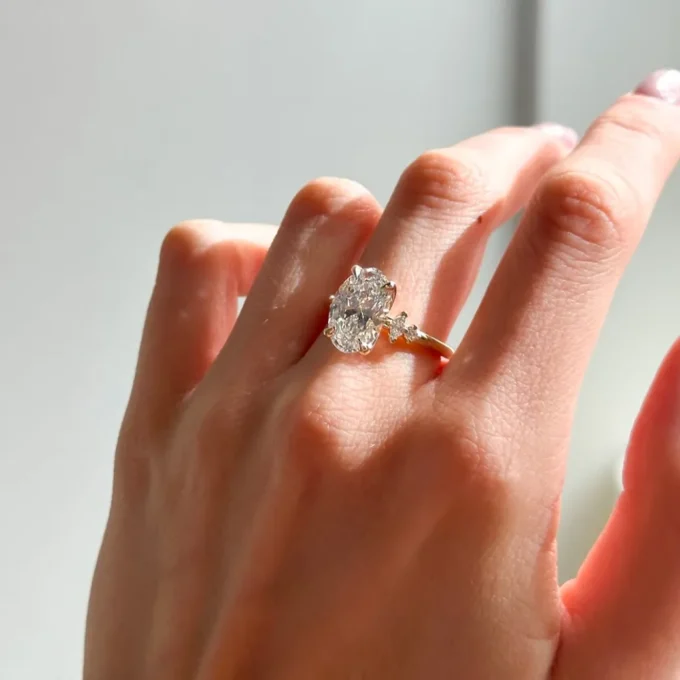 Sunlit close-up of a hand showcasing an oval-cut diamond solitaire on a delicate gold band, highlighting sparkle, clarity and refined craftsmanship.