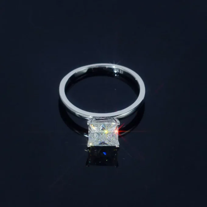 Princess-cut diamond solitaire engagement ring in white gold, sparkling on a glossy black surface with subtle reflections; elegant bridal jewelry.