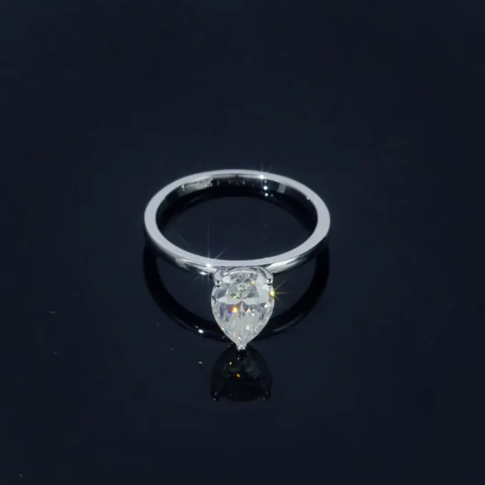 Pear-cut diamond solitaire ring in white gold, photographed on a glossy black surface. Elegant engagement jewelry with brilliant sparkle.